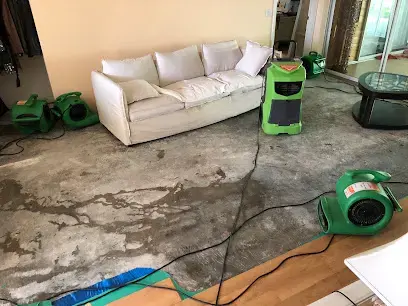 Air movers and a dehumidifier drying a bare slab in a North Port living room