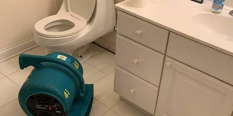 Air mover drying a bathroom floor beside a toilet after an overflow